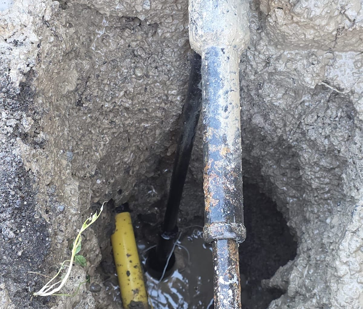 Leaning water curb box exposed in a hydrovac hole with the tracer wire and valve riser visible