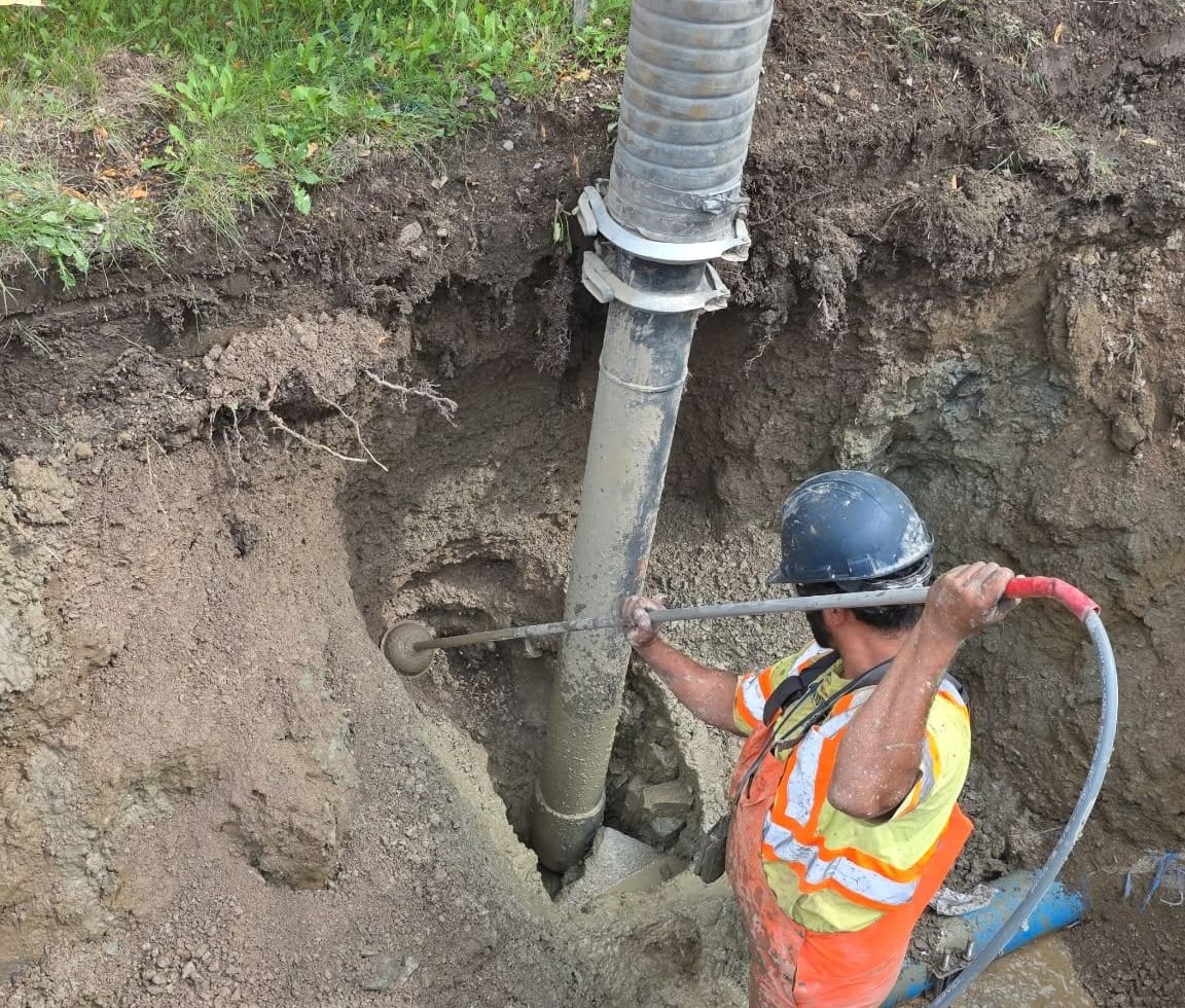 Operator in a hard hat guiding the hydrovac hose and wand to expose a buried line in a test pit