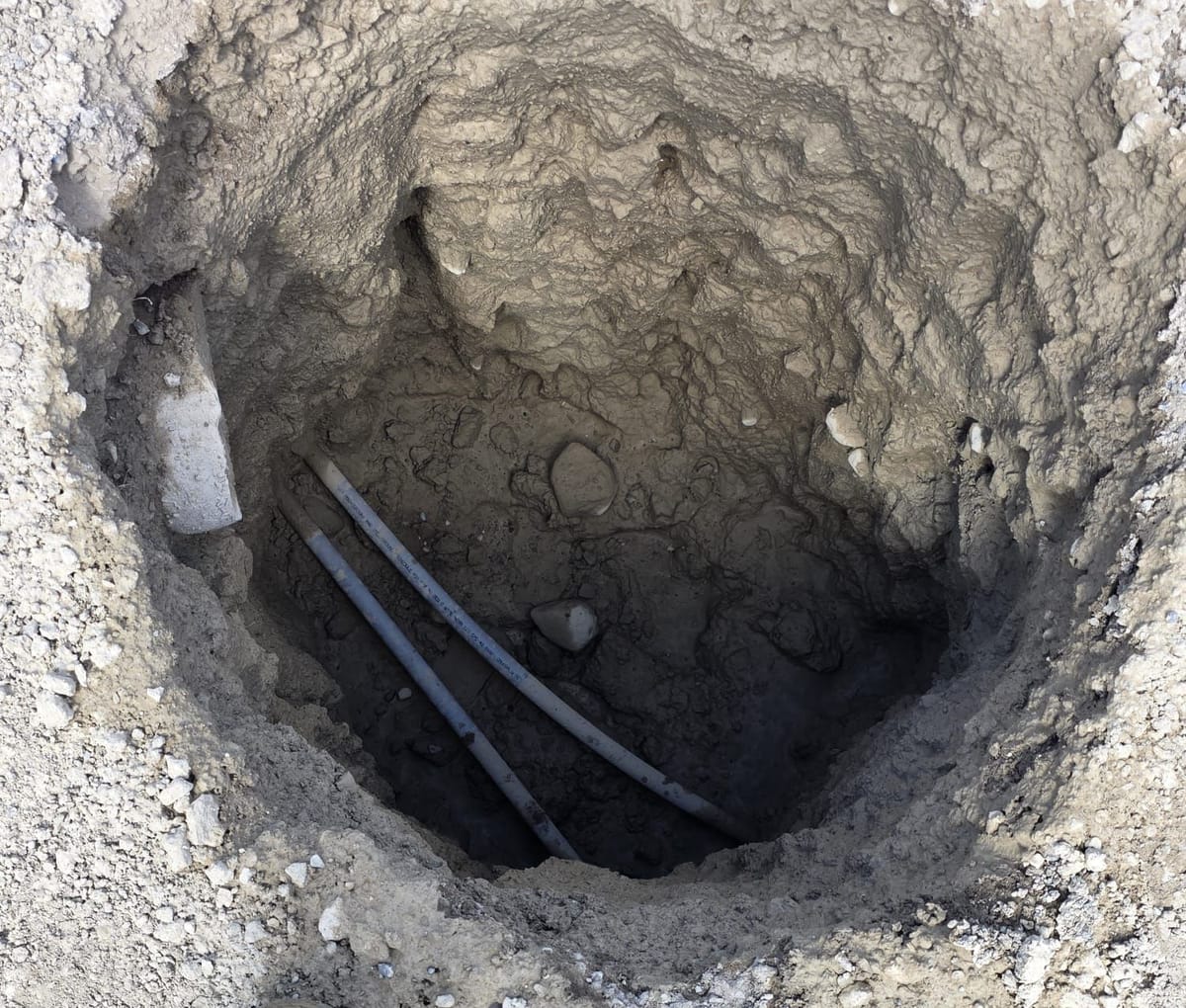 Round hydrovac test hole with two buried cables exposed and undamaged at the bottom