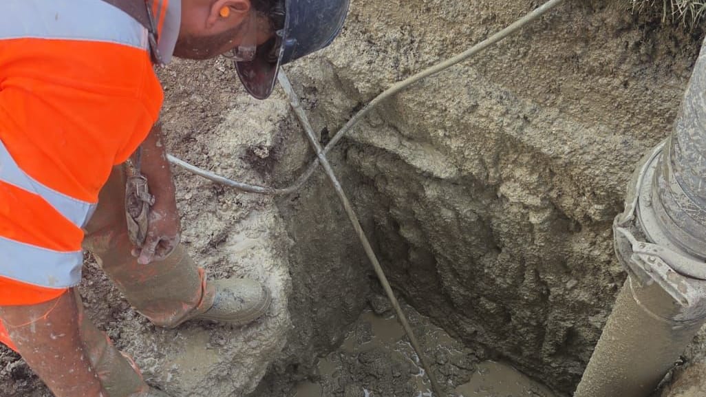 Operator measuring the depth of exposed buried cables in a hydrovac test hole with a tape