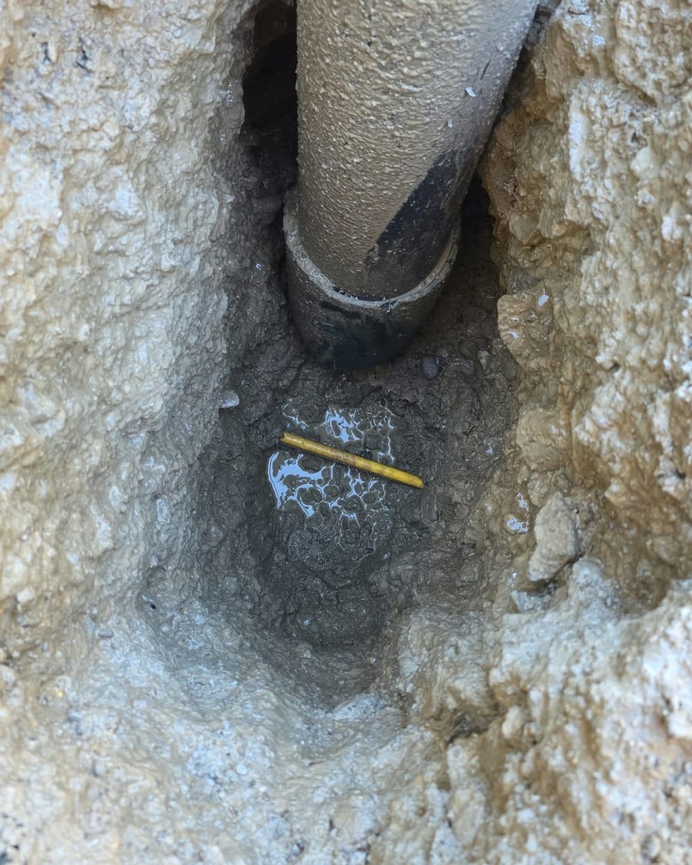 Vertical valve riser pipe exposed undamaged in a tight hydrovac test hole in grey clay