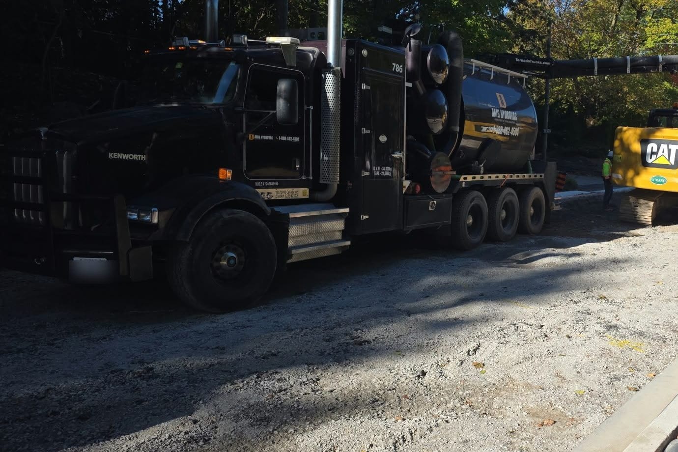 AMG Hydrovac truck on a road reconstruction site with its boom extended beside a CAT excavator, the crew digging alongside