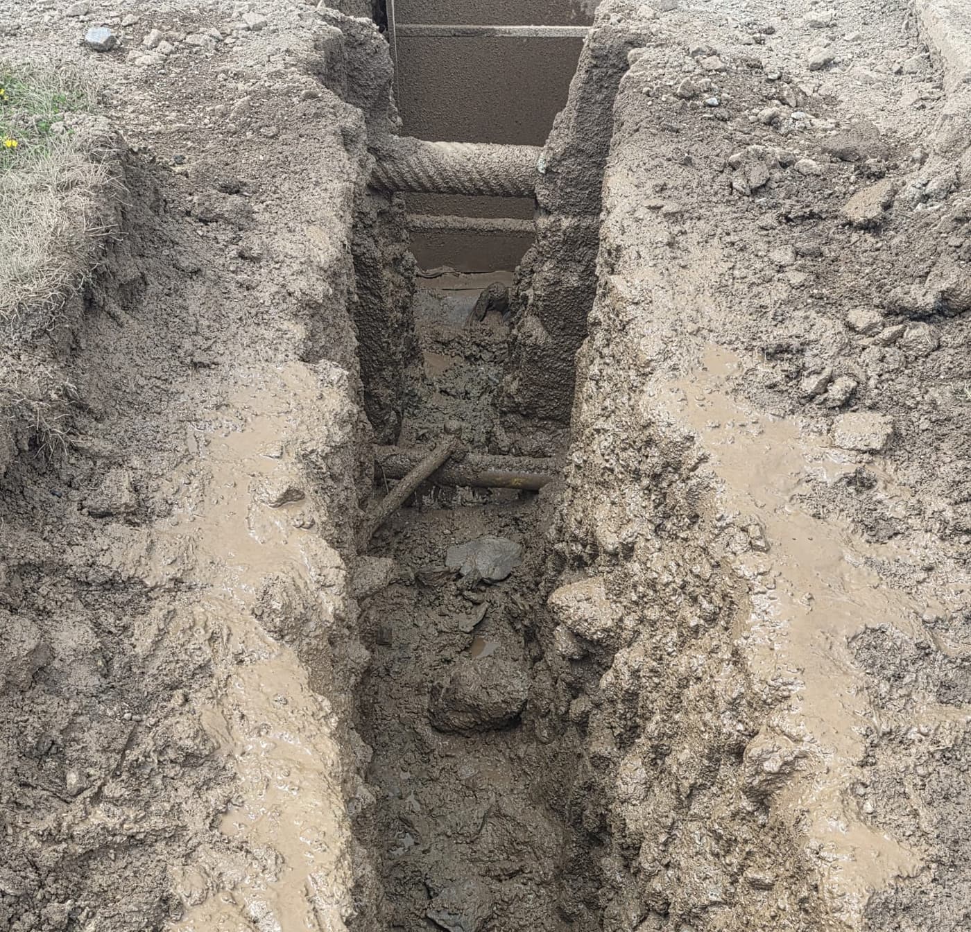 Narrow hydrovac slot trench with clean vertical walls cut between a road and sidewalk, existing service line exposed and intact